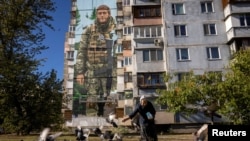 ARCHIVO - Una mujer alimenta palomas frente a un mural del artista callejero ucraniano Eugene Gladenko que muestra al soldado ucraniano caído Maksym Bordus, en medio del ataque de Rusia a Ucrania, en Kiev, Ucrania, el 8 de octubre de 2024.