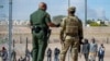 Migrantes aguardan a un costado del muro fronterizo vigilado por la Patrulla Fronteriza y la Guardia Nacional de Texas el miércoles 10 de mayo de 2023, con el fin de ingresar a El Paso, Texas.