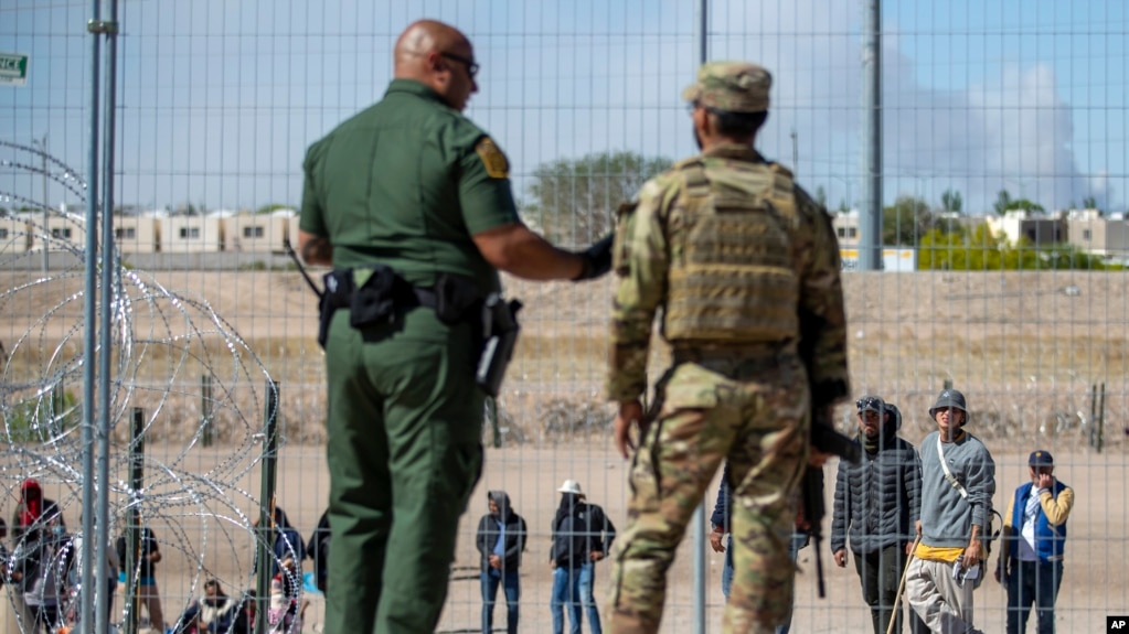 Migrantes aguardan a un costado del muro fronterizo vigilado por la Patrulla Fronteriza y la Guardia Nacional de Texas el miércoles 10 de mayo de 2023, con el fin de ingresar a El Paso, Texas.