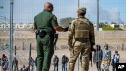 Migrantes aguardan a un costado del muro fronterizo vigilado por la Patrulla Fronteriza y la Guardia Nacional de Texas el miércoles 10 de mayo de 2023, con el fin de ingresar a El Paso, Texas.