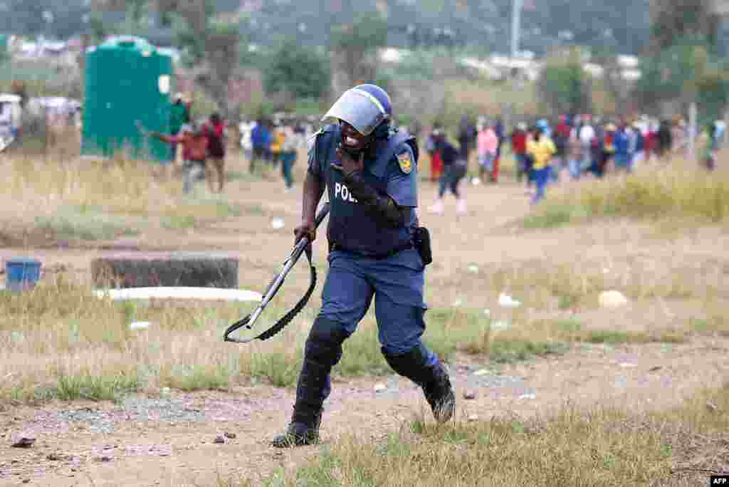 A South African Police Services member reacts after he was hit by a rock during a demonstration of Gomora informal settlement community members to protest against the lack of service delivery or basic necessities such as access to water and electricity, housing difficulties and lack of public road maintenance in Pretoria.