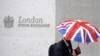 FILE - A worker shelters from the rain under a Union Flag umbrella as he passes the London Stock Exchange in London, Britain.