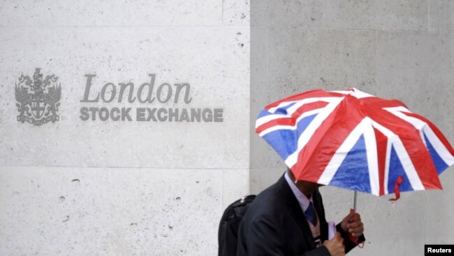 FILE - A worker shelters from the rain under a Union Flag umbrella as he passes the London Stock Exchange in London, Britain.