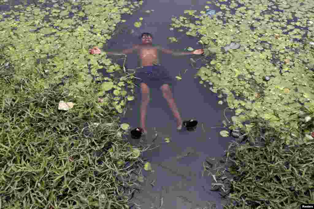 A boy floats in a pond to cool off on a hot summer day on the outskirts of Kolkata, India.