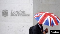 FILE - A worker shelters from the rain under a Union Flag umbrella as he passes the London Stock Exchange in London, Britain.