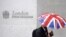 FILE - A worker shelters from the rain under a Union Flag umbrella as he passes the London Stock Exchange in London, Britain.