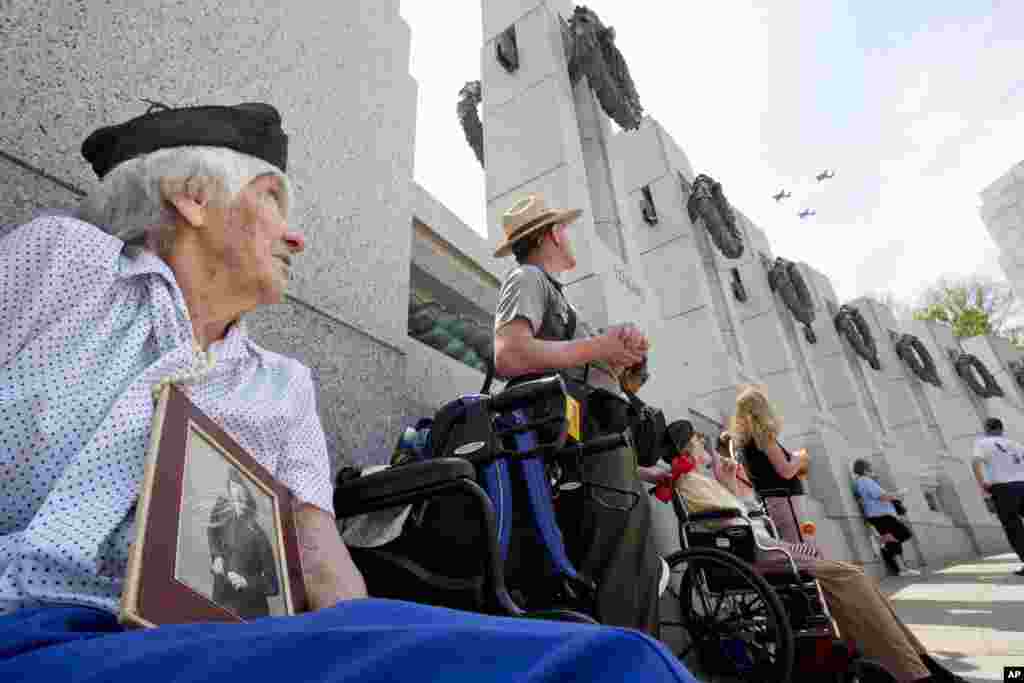 Holding a World War II-era photograph of herself, WWII veteran Elizabeth Copp, 96, who was a Sergeant in the Women&#39;s Army Corps during World War II, watches as World War II aircraft fly over the World War II Memorial in Washington, May 8, 2015, in honor of the 70th anniversary of Victory in Europe Day (VE Day).