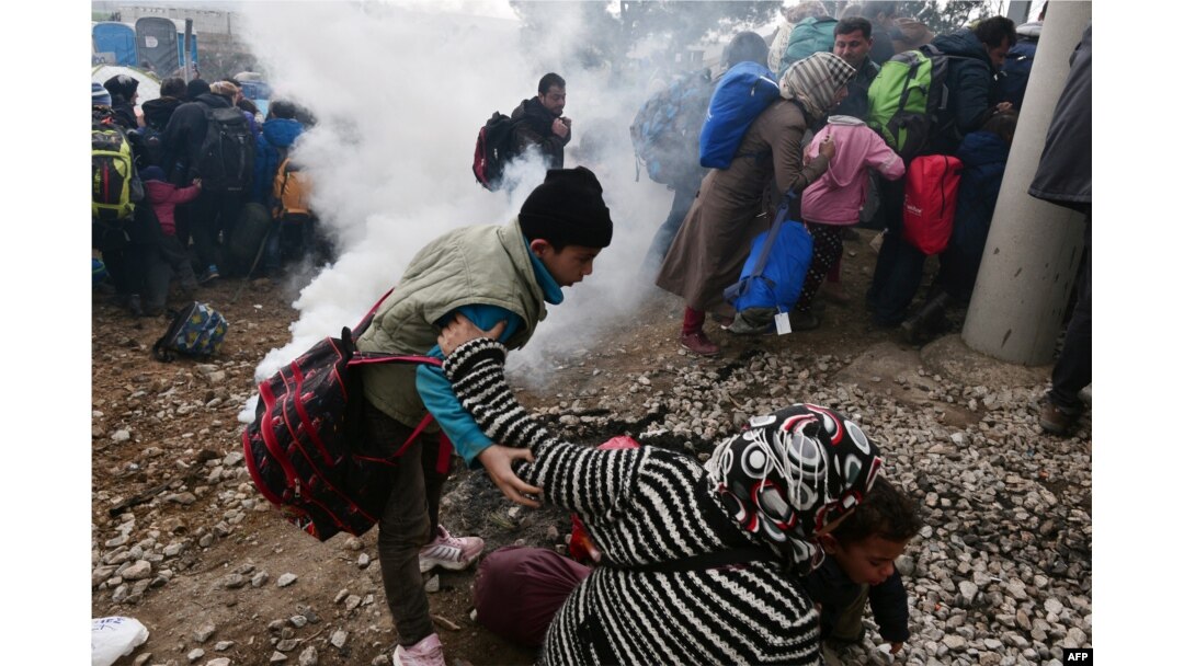 A woman falls as refugees with their children run away after Macedonian police used tear gas to dispearse refugees trying to break the gate to enter Macedonia, Feb. 29, 2016.