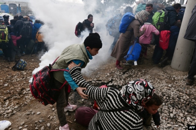 A woman falls as refugees with their children run away after Macedonian police used tear gas to dispearse refugees trying to break the gate to enter Macedonia, Feb. 29, 2016.