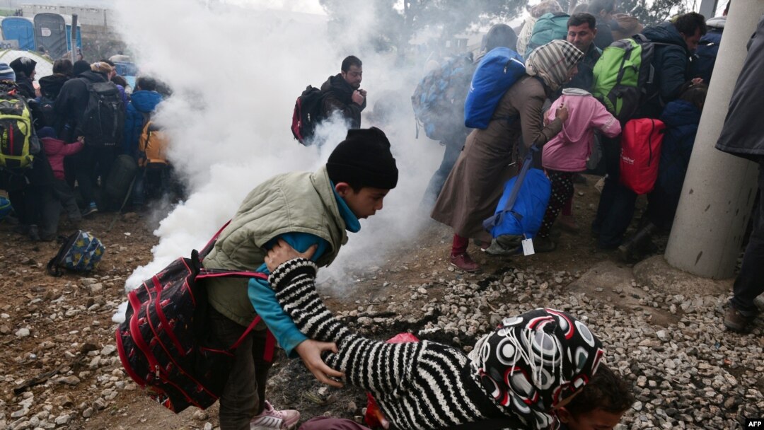 A woman falls as refugees with their children run away after Macedonian police used tear gas to dispearse refugees trying to break the gate to enter Macedonia, Feb. 29, 2016. 