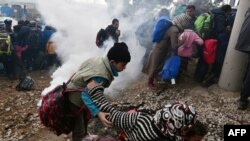 A woman falls as refugees with their children run away after Macedonian police used tear gas to dispearse refugees trying to break the gate to enter Macedonia, Feb. 29, 2016. 