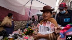 Una mujer lleva artículos en miniatura y dinero falso que compró en la Feria anual de Alasita en La Paz, Bolivia, el lunes 24 de enero de 2022. (AP Foto/Juan Karita)