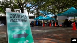 FILE - People wait in line to get tested for COVID-19, at rear, as a sign points to an empty vaccination tent outside the Stephen P. Clark Government Center building, Dec. 22, 2021, in downtown Miami. 