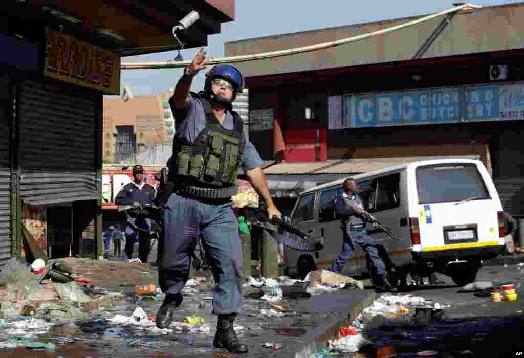 A riot police officer throws a tear gas canister as looters make off with goods from a store in Germiston, east of Johannesburg, South Africa, Sept. 3, 2019. 