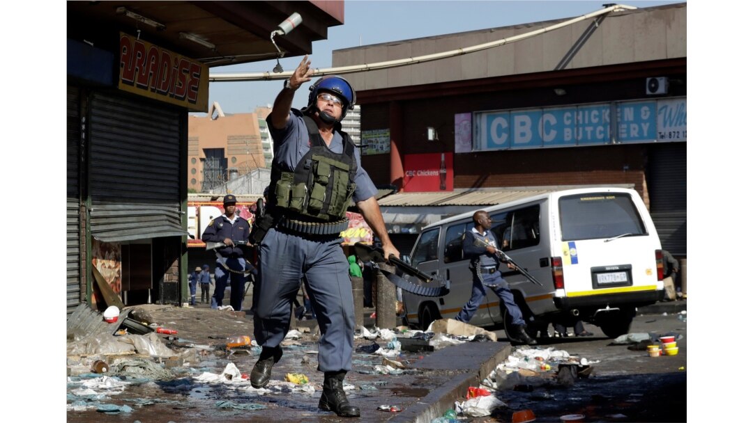 A riot police officer throws a tear gas canister as looters make off with goods from a store in Germiston, east of Johannesburg, South Africa, Sept. 3, 2019.