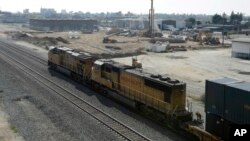 FILE - A freight train passes one of the construction sites for the California High-Speed Rail Train, in Fresno, Calif., Feb. 26, 2016. State lawmakers will have their first opportunity to quiz the officials responsible for California's $64 billion high-speed rail plans at a committee hearing Monday to review a new business plan that calls for overhauling its proposed route and postponing the first service by three years.