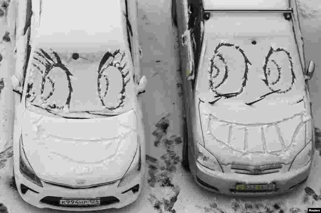 Faces are scrawled on cars covered with snow near a residential building in Krasnoyarsk, Russia.
