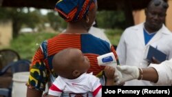 Seorang petugas kesehatan memeriksa suhu bayi yang memasuki Mali dari Guinea di perbatasan di Kouremale, 2 Oktober 2014. Seorang perempuan Mali melahirkan sembilan bayi pada 4 Mei 2021.(Foto: REUTERS/Joe Penney)