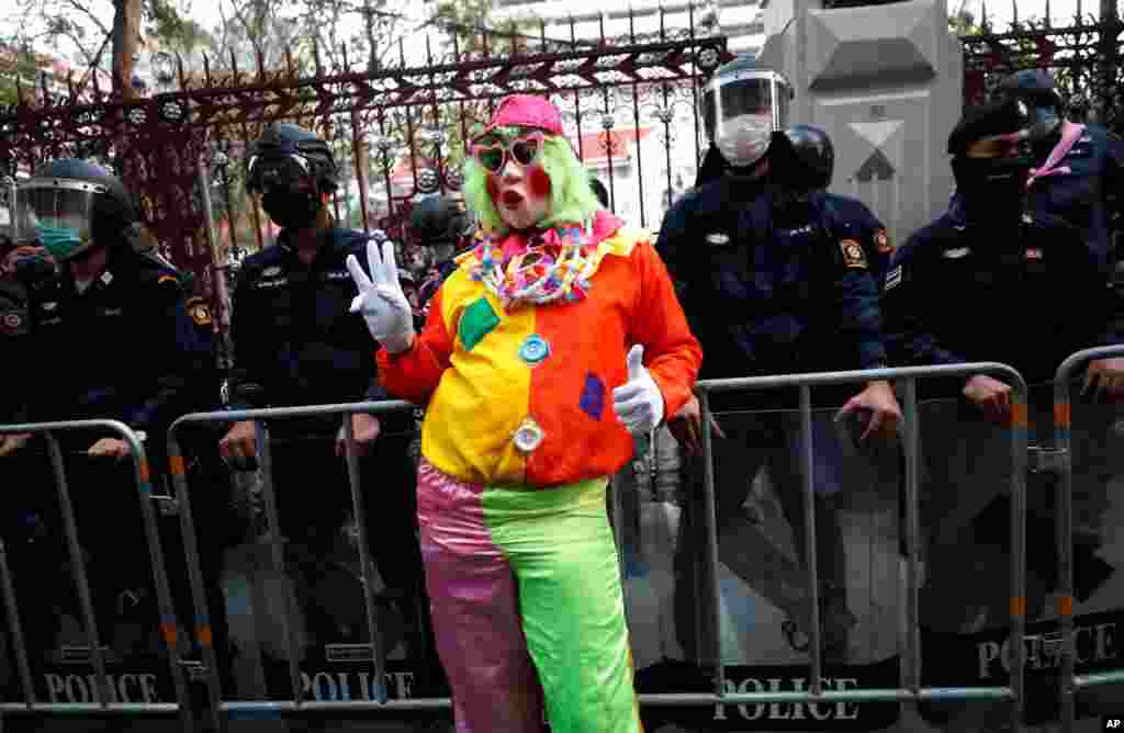 A pro-democracy protester wearing a clown costume raises a three-finger salute in front of riot police at Police Headquarter in Bangkok, Thailand. Protesters gathered to call for fairness for low-ranking police officers.
