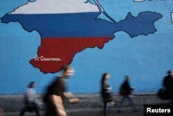 FILE - People pass a mural showing a map of Crimea in the Russian national colors on a street in Moscow, March 25, 2014.