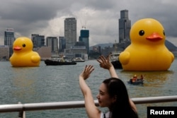 A woman poses for a photo as an art installation, dubbed "Double Ducks" by Dutch artist Florentijn Hofman, is seen in the background at Victoria Harbor. (REUTERS/Tyrone Siu)