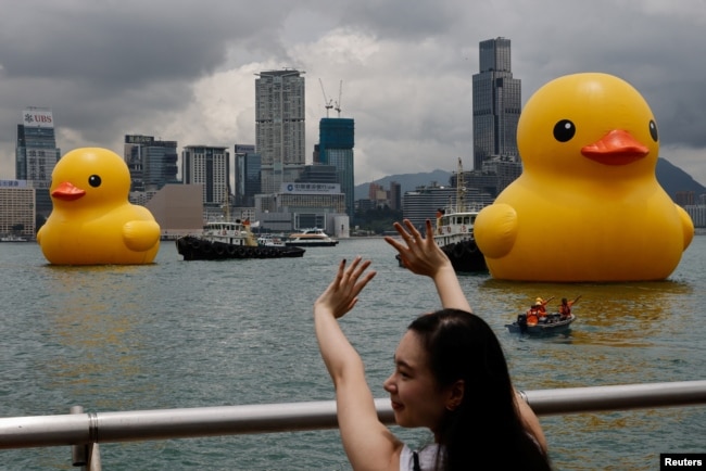 A woman poses for a photo as an art installation, dubbed "Double Ducks" by Dutch artist Florentijn Hofman, is seen in the background at Victoria Harbor. (REUTERS/Tyrone Siu)