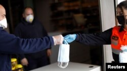 Petugas membagikan masker di luar sebuah toko makanan saat berlangsungnya karantina akibat wabah corona di Ronda, Spanyol, 13 April 2020. 