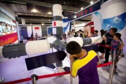 FILE - Visitors look at a model of China's Tiangong-1 space station at the China Beijing International High-Tech Expo in Beijing, June 10, 2017.