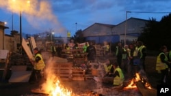 Demonstrators stand in front of a makeshift barricade set up by the so-called yellow jackets to block the entrance of a fuel depot in Le Mans, western France, Tuesday, Dec. 5, 2018. 