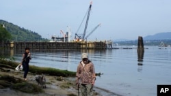 A couple walk their dog on the shore near the Kinder Morgan Inc. Westridge oil tanker terminal in Burnaby, British Columbia, Canada, May 3, 2018.