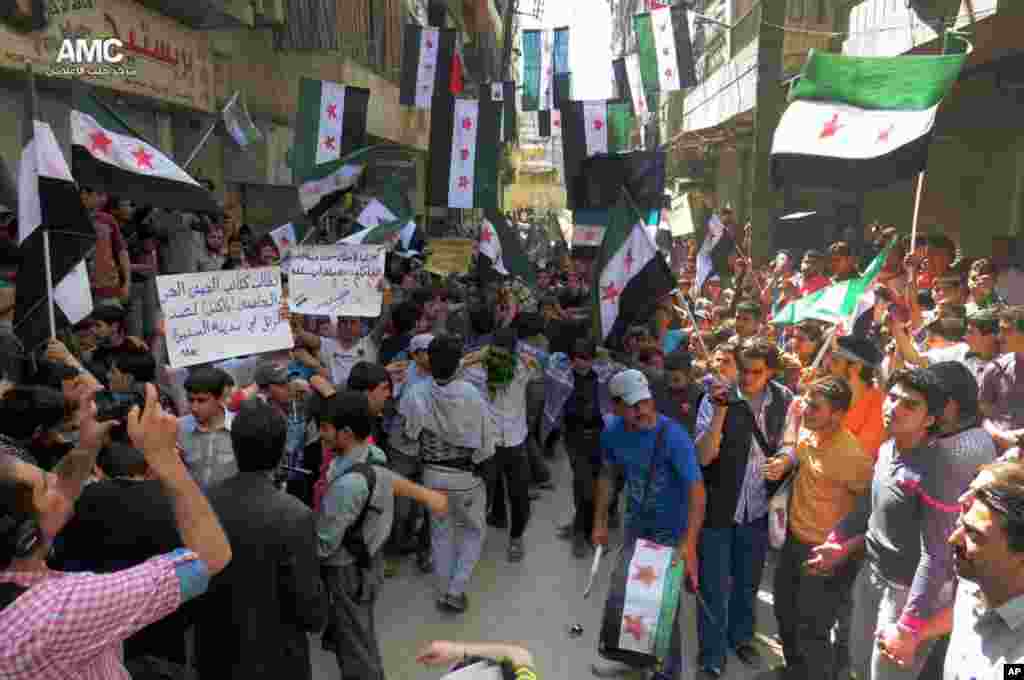This citizen journalism image shows anti-Syrian regime protesters holding banners and waving the Syrian revolutionary flags, Aleppo, Syria, April 26, 2013. (Aleppo Media Center AMC)
