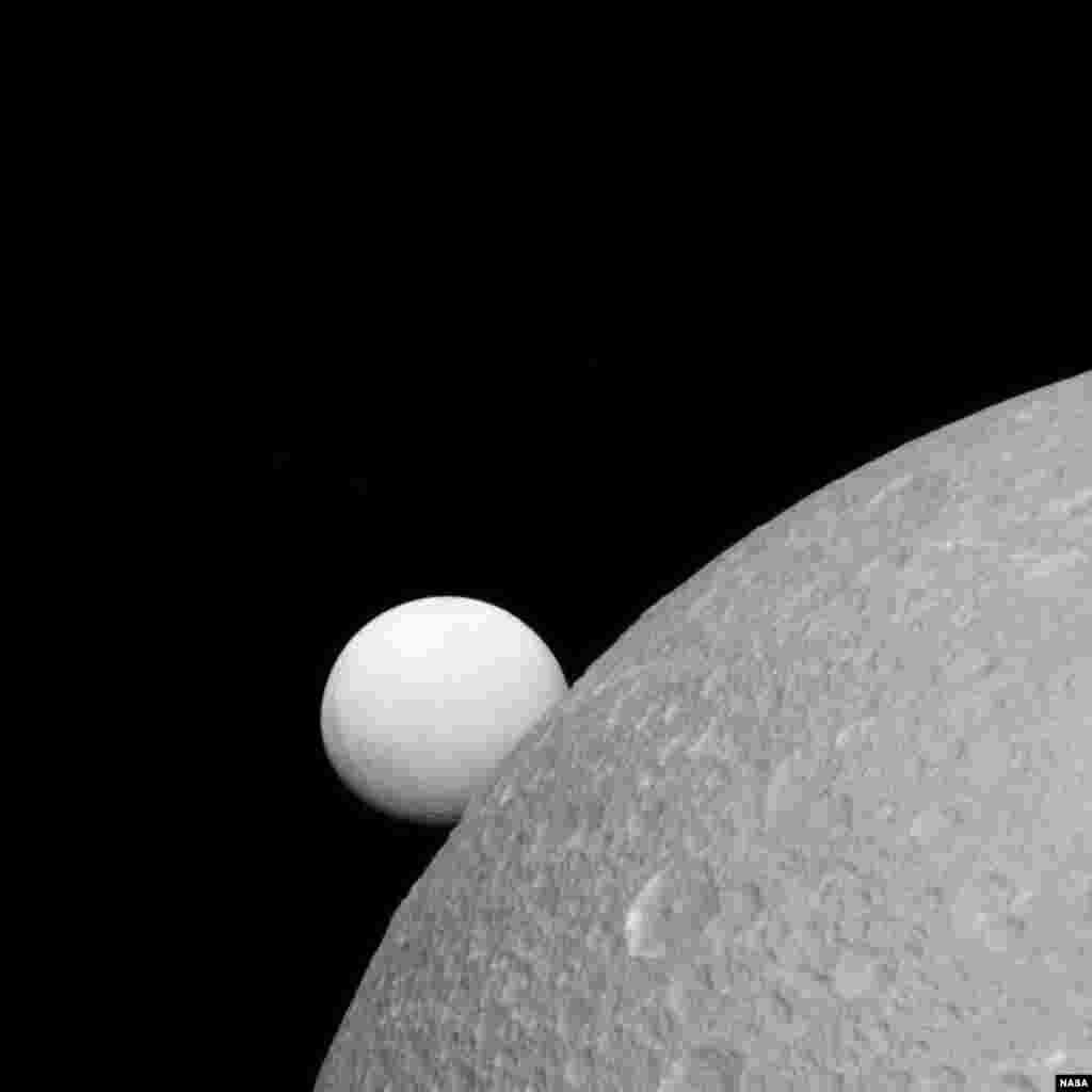 Dione with Enceladus in the background. This image was taken by the Cassini spacecraft, Sept. 8, 2015.