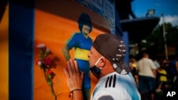 A soccer fan kisses a poster of Diego Maradona at the entrance of the Boca Juniors stadium, known as La Bombomera, in Buenos Aires, Argentina, Nov. 25, 2020. 
