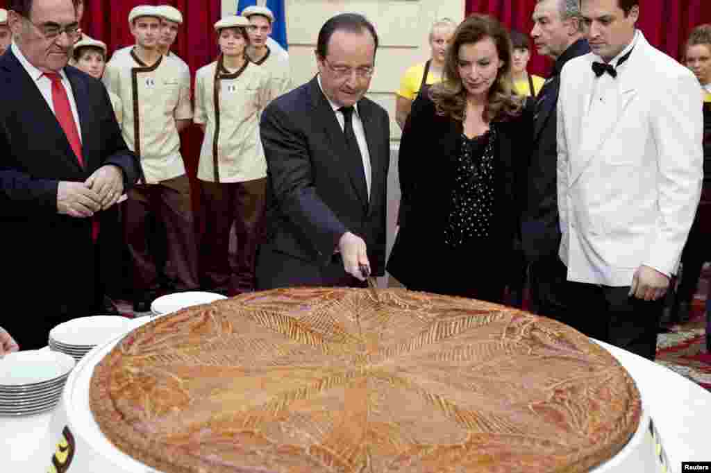 French President Francois Hollande (C) and his companion Valerie Trierweiller cut a giant traditional Epiphany cake during a ceremony at the Elysee Palace in Paris.