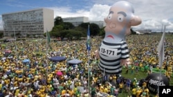 ພວກປະທ້ວງ ຮຽກຮ້ອງໃຫ້ປົດປະທານາທິບໍດີ ຂອງ ບຣາຊິລ ທ່ານນາງ Dilma Rousseff ອອກຈາກຕຳແໜ່ງ, ໃນລະ
ຫວ່າງການຊຸມນຸມທີ່ມີໂຕກາຕູນອັດລົມຂອງ ອະດີດປະ
ທານາທິບໍດີ Luiz Inacio Lula da Silva ຢືນຢູ່ໃນຊຸດ
ນັກໂທດ ທີ່ນະຄອນຫຼວງ Brasilia, ປະເທດ ບຣາຊິລ.13 ມີນາ, 2016.