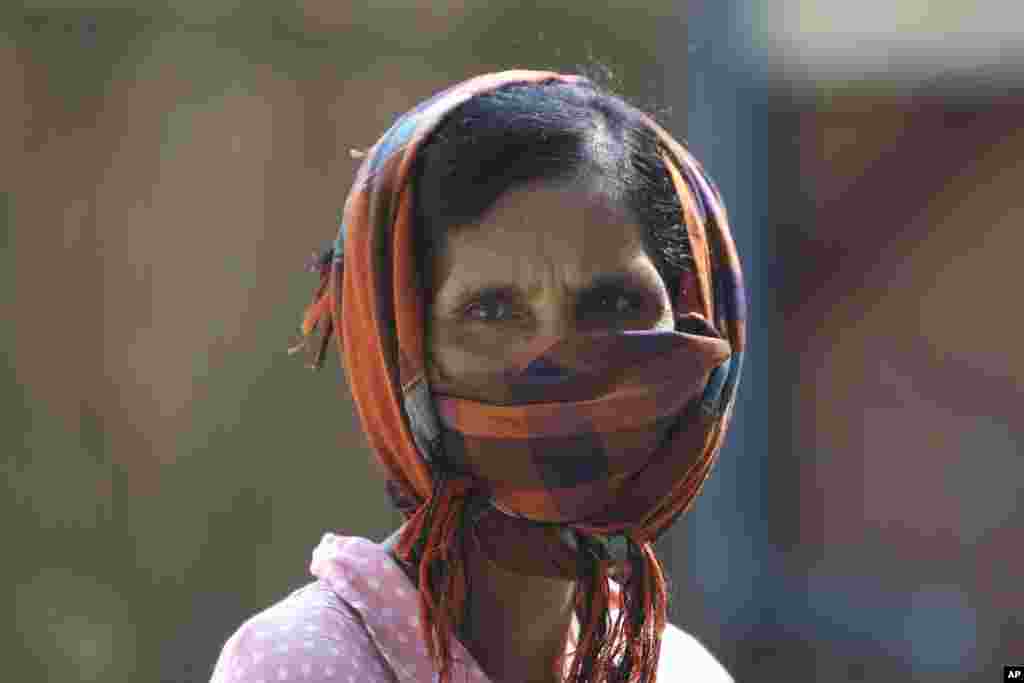 A woman uses a headscarf as a protective mask while watching staff from the Cambodian Children's Fund spray disinfectant to help curb the spread of the new coronavirus in the slum neighborhood of Stung Meanchey in southern Phnom Penh, Cambodia, Tuesday, March 24, 2020. (AP Photo/Heng Sinith)