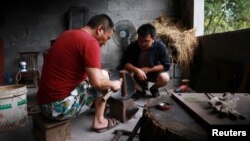 Owner Tian Huan (R) chats with a blacksmith at his workshop for handmade woks in Datian village, Hubei province, China August 13, 2018. 