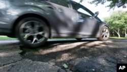 FILE - An automobile drives over a pothole in Bloomfield Township, Michigan.