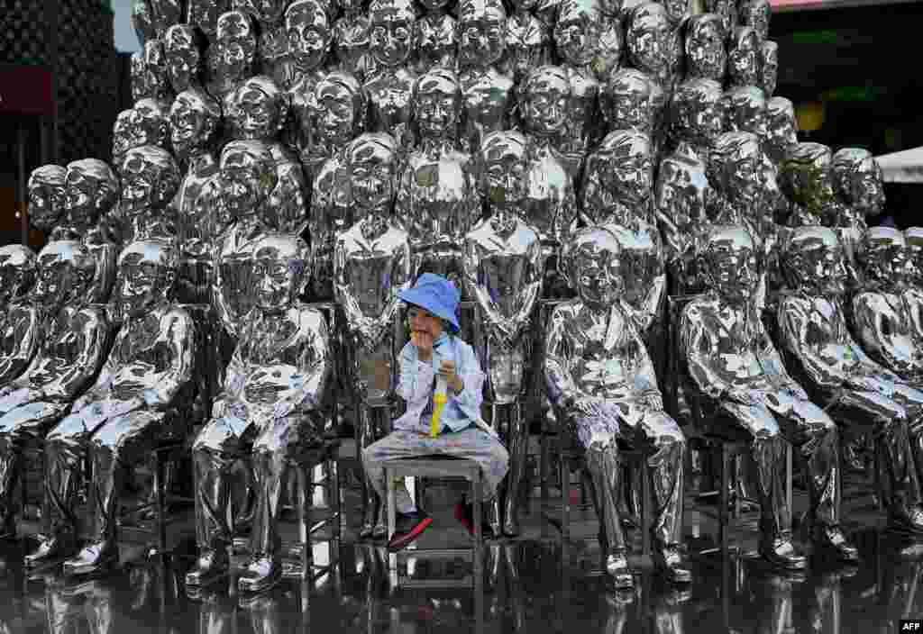 중국 베이징의 한 쇼핑센터에서 어린이 모양의 조형물 사이에 소년이 앉아있다.
