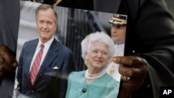 FILE - Lucy Orlando from Florida hold up a photo of Former President George H. W. Bush and his wife Barbara Bush as she waits for the visitation of the former first lady, April 20, 2018, in Houston, Texas.