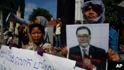 A Cambodian opposition party supporter, right, holds a portrait photo of an opposition senator Hong Sok Hour during a protest in front of the Phnom Penh Municipal Court, in Phnom Penh, Cambodia, Saturday, Aug. 15, 2015. Cambodian authorities arrested an opposition senator Saturday, two days after Prime Minister Hun Sen accused him of treason for comments posted on Facebook. A slogan reads: free senator Hong Sok Hour. (AP Photo/Heng Sinith)