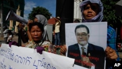 A Cambodian opposition party supporter, right, holds a portrait photo of an opposition senator Hong Sok Hour during a protest in front of the Phnom Penh Municipal Court, in Phnom Penh, Cambodia, Saturday, Aug. 15, 2015. 