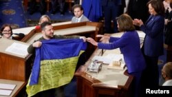 Ukraine's President Volodymyr Zelenskyy presents a Ukrainian flag given to him by defenders of Bakhmut to U.S. House Speaker Nancy Pelosi (D-CA), while U.S. Vice President Kamala Harris applauds during a joint meeting of U.S. Congress in the House Chamber of the U.S. Capitol in Washington, Dec. 21, 2022.