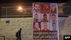 FILE - A man walks by a banner depicting the six Palestinian prison escapees, in the West Bank town of Bethlehem, September 8, 2021.