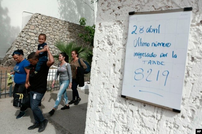 Cuban migrants line up to be called by Mexican immigration officials in Ciudad Juarez, Mexico, to be taken across the Paso del Norte International bridge to be processed as asylum-seekers on the U.S. side of the border, April 29, 2019. The sign on the wall reads in Spanish "April 28 The last number called in the afternoon is 8219."