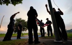 Los bomberos de Port Arthur, Texas, bajan una bandera estadounidense en una oficina de correos al atardecer mientras esperan que el huracán Laura toque tierra.