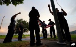 Los bomberos de Port Arthur, Texas, bajan una bandera estadounidense en una oficina de correos al atardecer mientras esperan que el huracán Laura toque tierra.