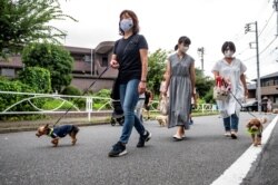 Anggota "Patroli Wan-Wan" lokal berjalan di sepanjang jalan menuju sebuah sekolah dasar di Tokyo, Jepang, 14 Juli 2021. (AFP)