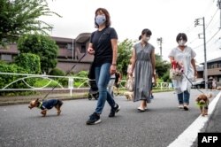 Anggota "Patroli Wan-Wan" lokal berjalan di sepanjang jalan menuju sebuah sekolah dasar di Tokyo, Jepang, 14 Juli 2021. (AFP)