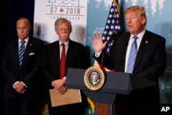 White House chief economic adviser Larry Kudlow, left, and national security adviser John Bolton look on as President Donald Trump speaks during a news conference at the G-7 summit, June 9, 2018, in La Malbaie, Quebec, Canada.